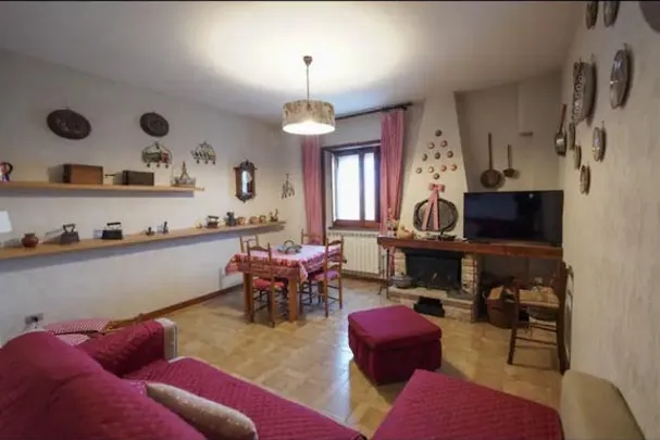 Bright living room with a red sofa, stone fireplace and dining area with a checked tablecloth